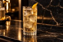Vaso de bebida carbonatada con hielo y piel de cítrico sobre una barra oscura