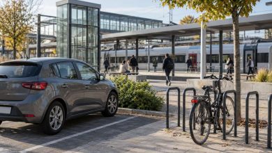 Coche estacionado y bicicleta en un intercambiador con un andén de tren visible al fondo.